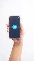 Yogyakarta, Indonesia, 2025 - Hand holding phone that shows front page of Telegram, messaging and communication platform application, on the screen isolated on white background photo