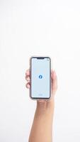 Yogyakarta, Indonesia, 2025 - Hand holding smartphone that shows front page of Facebook application, a social networking service platform, on screen isolated on white background photo