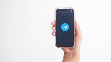 Yogyakarta, Indonesia, 2025 - Hand holding phone that shows Telegram icon, messaging and communication platform application, on the screen isolated on white background photo