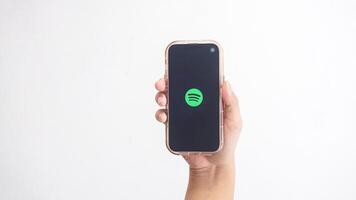 Yogyakarta, Indonesia, 2025 - Hand holding smartphone that shows Spotify icon, digital audio streaming platform application, on the screen isolated on white background photo