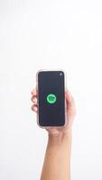 Yogyakarta, Indonesia, 2025 - Hand holding smartphone that shows front page of Spotify, digital audio streaming platform application, on the screen isolated on white background photo