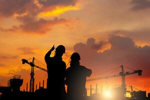 Silhouette of Engineer and worker checking project at building site background, Worker showing thumbs up construction site at sunset in evening time photo