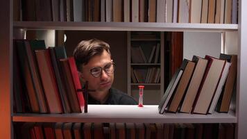 Young theologian contemplating a red hourglass surrounded by books and a cross in a library, representing the intricate relationship between time, faith, and knowledge video