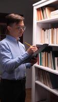 A man in glasses is holding a clipboard while standing in front of a bookcase video