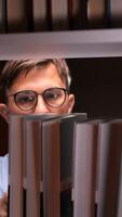vertical Male librarian with eyeglasses searching books on a shelf in a library or bookstore, looking for specific title for customer or for himself video