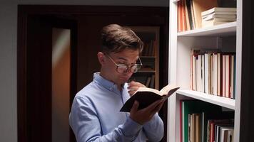 A man in glasses is reading a book in a library video