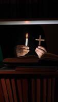 A person holding a lit candle and a cross in front of a book video