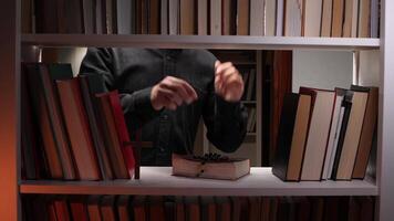Priest holding reading glasses with a holy bible, rosary beads, and small wooden cross displayed on a white bookshelf filled with books in a library video