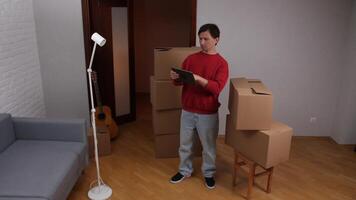 Man using digital tablet while organizing new home with cardboard boxes video