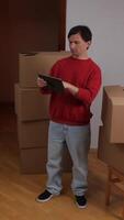 vertical close-up Man using digital tablet while organizing new home with cardboard boxes video