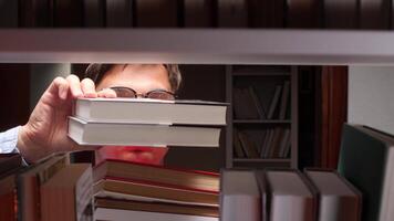 University student wearing glasses is selecting books in the college library, diligently searching for valuable information to support his research project and academic pursuits video