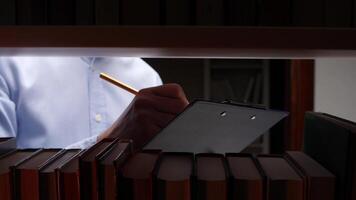 A man is writing on a clipboard in front of a book shelf video
