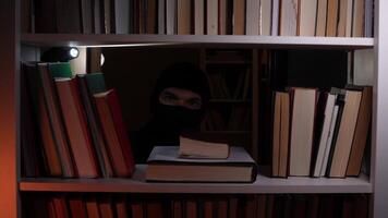 A person in a black mask is looking through a bookcase video