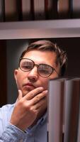 vertical University student wearing glasses, contemplating which book to select while surrounded by towering bookshelves in a bustling college library, immersed in the pursuit of knowledge video