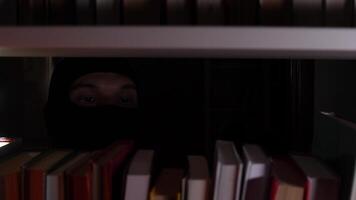A person in a black mask is hiding behind a book shelf video