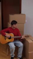 vertical close-up Man playing acoustic guitar in new apartment after moving in video
