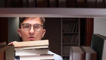 Young college student searching for books in a university library, holding a stack of literature while intently examining the bookshelf, embodying the spirit of education and learning video