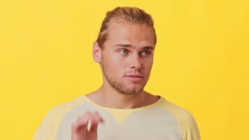 A young man of mixed heritage shows curiosity by cupping his hand behind his ear. He stands out against a bold yellow background, capturing a moment of engagement and interest. video