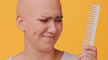 A cheerful young woman with a shaved head poses confidently while holding a comb. She has a warm smile and stands against a vibrant yellow background, showcasing her unique style and confidence. video