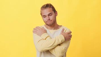 A young man with mixed African and Caucasian features stands against a vibrant yellow backdrop. He wraps his arms around himself, reflecting a contemplative mood as he gazes downward. video