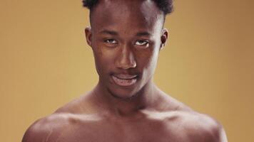 A young African American man stands quietly, gazing downwards with a contemplative expression. The background features a soft, warm hue that enhances the intimate atmosphere. video