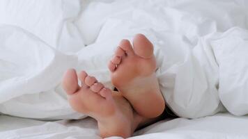 In a serene morning setting, a woman relaxes in bed, her feet peeking out from under the soft, white sheets, creating a calm and peaceful atmosphere. video