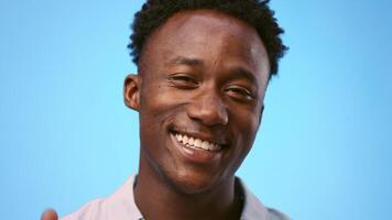 A young African American man displays a happy expression while facing the camera, showing thumbs up. The plain blue background highlights his features and confident demeanor video