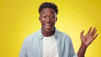A young African American man stands confidently, smiling widely against a vibrant yellow backdrop. His relaxed demeanor and expressive smile convey happiness and warmth. video
