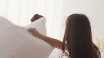 Two friends are playfully engaging in a pillow fight in a brightly lit room. The sunlight streams through the curtains, creating a cheerful atmosphere as they laugh and have fun. video