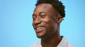 A young African American man is expressing joy and engagement with a cheerful smile. The vibrant blue background enhances the lively atmosphere of the moment, copy space video