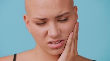 A young bald woman with striking features shows a serious expression while resting her hand on her cheek, experiencing toothache video