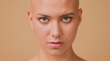 A young woman with a completely bald head showcases a strong expression, captivating the viewer with her intense gaze. The neutral background enhances her features and confidence. video