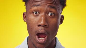 A young African American man gazes directly at the viewer, showcasing a calm yet serious demeanor. His backdrop features a vibrant yellow hue, enhancing his focused expression. video