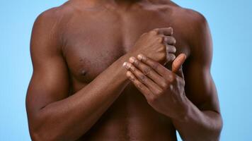 A millennial man with a smooth complexion is applying lotion on his forearm, suffering from sprain. The bright blue background video