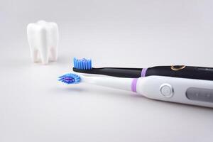 The white and black electric ultrasonic toothbrushes on a gray surface. photo