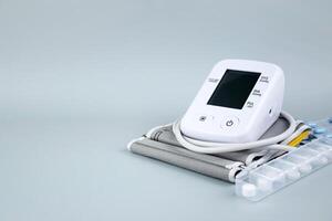 Digital blood pressure tonometer and pack of pills on the blue background with copy space. photo