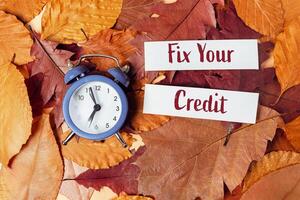Clock surrounded by autumn leaves with Fix Your Credit written on paper symbolizing financial change and urgency photo