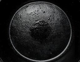 minimalist top view of cast iron skillet surface with subtle oily center and moody black texture background for cooking or kitchen design photo