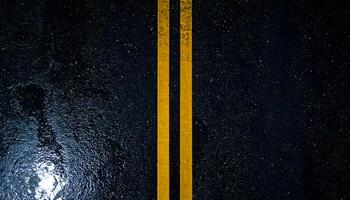 wet asphalt road at night with double yellow lines, top view of dark moody street texture with rain reflections and urban atmosphere photo
