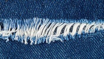 close-up frayed denim fabric with torn white threads, top view macro of distressed blue jeans texture for fashion or textile background photo