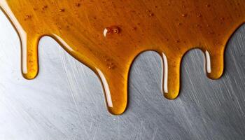 dripping honey on metal surface close-up, golden syrup flowing with glossy texture and warm highlights, macro food design background for sweet dessert or healthy ingredient concept photo