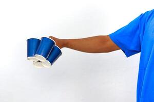 A hand holds a bunch of blue disposable cups against a white background, ready for a picnic or party photo