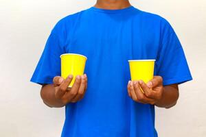Person in blue shirt holding two yellow cups, possibly for a beverage or food sampling demo photo