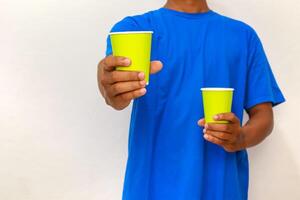 Person in blue shirt holding two yellow paper cups, offering one forward to the viewer photo