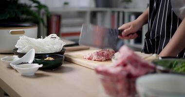Handheld focus shot, Asian woman's hands is chopping pork on a wooden cutting board to prepare for cooking. video