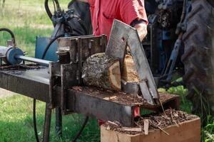 Farmer splitting firewood logs using tractor driven log splitter machine photo