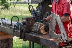 Farmer splitting firewood logs using tractor driven hydraulic log splitter machine photo