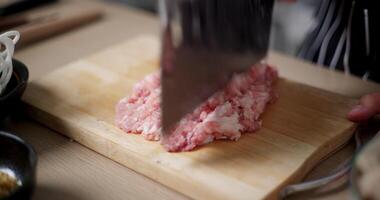 Handheld selective focus shot, Asian woman's hands is chopping pork on a wooden cutting board to prepare for cooking. video