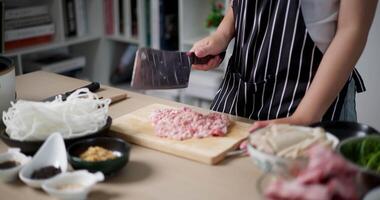 Handheld selective focus shot, Asian woman's hands is chopping pork on a wooden cutting board to prepare for cooking at home. video