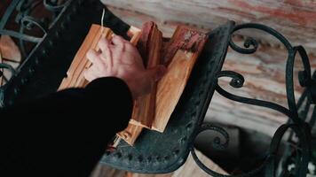 POV shot. man hand lifting seasoned firewood from metal rack, revealing rich wood texture and graceful movement in slow motion capturing rustic preparation. Hand grabbing firewood from wooden rack video